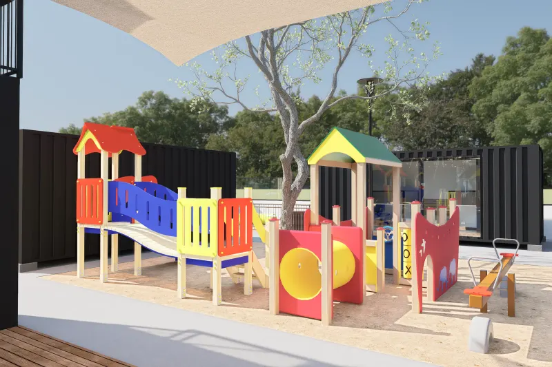 Parque infantil com escorregas coloridos em caixa de areia junto a contentores.