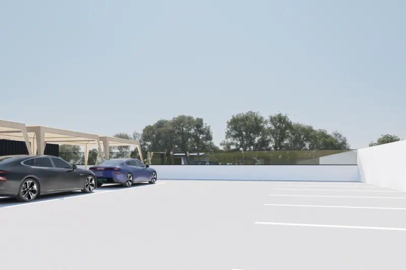 Parque de estacionamento exterior do complexo com viaturas e árvores ao fundo.